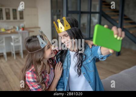 Mutter und Tochter tragen Kronen und machen selfie Stockfoto