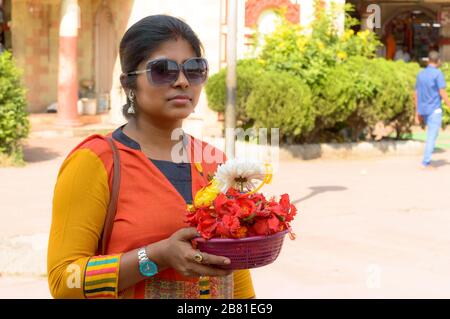 Lächelndes Porträt der schönen jungen Erwachsenen traditionelle verheiratete bengalische Frau, die während Durga Puja celebrati einen Eimer religiöser Blumen anbietet Stockfoto