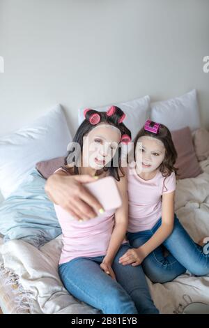 Mutter und Tochter mit Gesichtsmaske auf den Gesichtern machen selfie Stockfoto