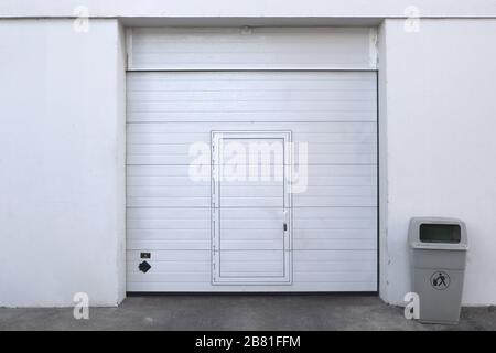 Geschlossene weiße Garage oder Lagerhalle mit Eingang und einem Behälter für Recycling Stockfoto