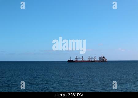 Frachtschiff, das im Sommer in einem ruhigen Meer mit klarem Himmel zu einem Hafen fährt Stockfoto