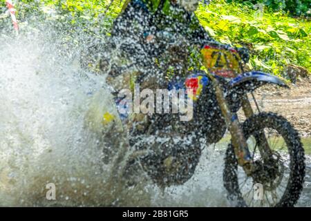 Sonniger Sommertag im Wald. Enduro-Athlet überwindet einen flachen Strom mit vielen Spritzern Stockfoto