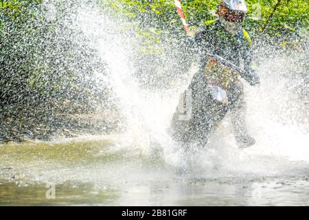 Sommersonntag im Wald. Enduro-Athlet überwindet einen flachen Strom mit vielen Spritzern Stockfoto