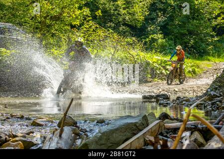 Sonniger Sommertag im Wald. Enduro-Athlet überwindet einen flachen Bach mit vielen Wasserspritzern Stockfoto