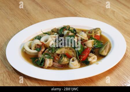 Gebratenes Rühren würzige Meeresfrüchte auf weißem Teller - Gericht am Holztisch, würzige Meeresfrüchte, würzige Speisen, Pad-cha Talay (thailändisches Wort) Stockfoto