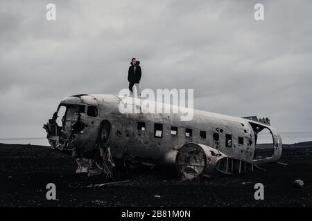 Berühmtes Flugzeugwrack in Island mit schwarzem Sand und einem Mann, der oben steht Stockfoto