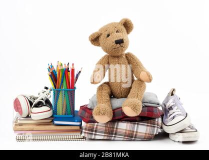 Stapel gefalteter Kleidung, Sport-Sneaker, Schreibwaren und ein brauner Teddybär auf weißem Hintergrund, Konzept zur Hilfe für Bedürftige, Spende Stockfoto