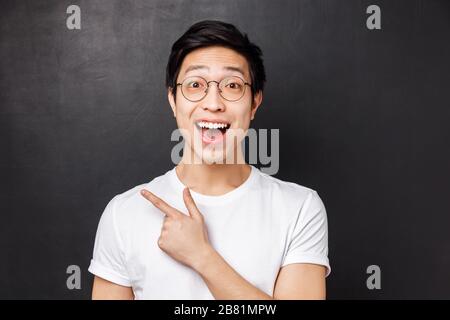 Nahaufnahme des begeisterten männlichen asiatischen Kollegen, der lebhafte Gespräche führt, Veranstaltungen oder neues Produkt auf Lager diskutiert und mit dem Finger oben links zeigt Stockfoto