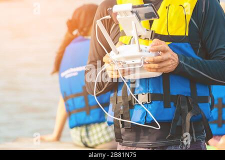 Junger Mann in blau-gelber Lebensweste, der eine Drohne kontrolliert, um mit Touristen auf einem Floß im Meer Bilder von der Küste des Ozeans zu machen. Hände h Stockfoto