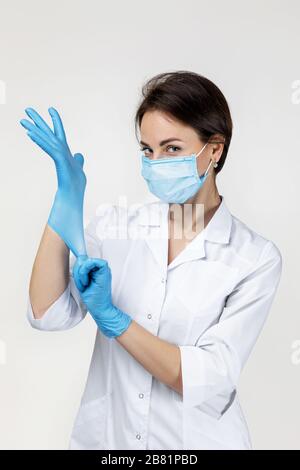 Junge Frau Doktor in weißer Uniform mit Maske und Gummihandschuhen auf grauem Hintergrund Stockfoto