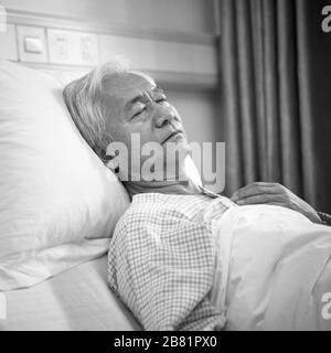 älterer asiatischer männlicher Patient, der im Bett liegt und in der Krankenstation oder der betreuten Wohneinrichtung schläft, schwarz-weiß Stockfoto
