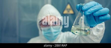 Wissenschaftler mit Schutzanzug, der im Labor auf das Reagenzglas blickt Stockfoto