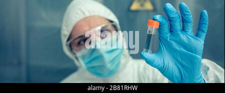 Wissenschaftler mit Schutzanzug, der im Labor auf die Durchstechflasche schaut Stockfoto