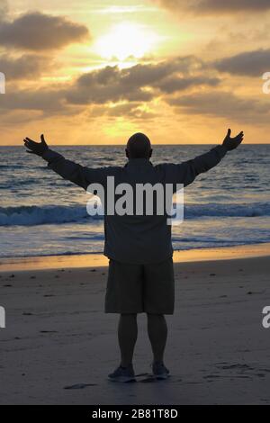 Ein Mann grüßt den Sonnenaufgang am Strand am Atlantik. Stockfoto