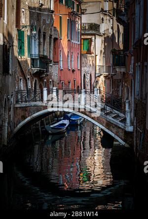 Leere Straßen Venedigs Italien mit einer im Wasser reflektierenden Frau und den traditionellen Häusern und Booten in den Kanälen Stockfoto