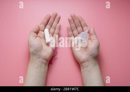 Frauen, die ein hygienisch-Menstruationsunterlage und Tampon halten. Choise-Konzept, Hygieneprodukte für Frauen. Flacher Lay, rosafarbener Hintergrund. Stockfoto