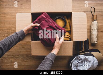 Reinigung von Heim- und Spendenkonzepten mit jungen Menschen, die Accessoires in brauner Schachtel legen.geben und mit human.second Hand- oder Recyclinghand teilen Stockfoto