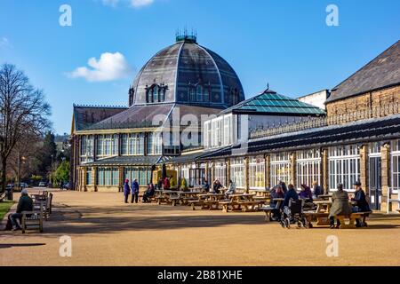 Leute, die draußen im Pavilion Gardens Buxton an einem sonnigen Wintertag sitzen und essen und trinken Stockfoto