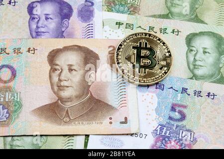 Nahaufnahme einer goldenen Bitcoin-Münze auf einem Stapel chinesischer Yuan-Banknoten. Stockfoto