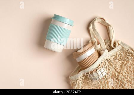 Saitenbeutel mit umweltfreundlichen Kaffeetassen zum Mitnehmen aus Bambus auf beigefarbenem Hintergrund. Kein Abfall, plastikfreies, nachhaltiges Lifestyle-Konzept. Stockfoto