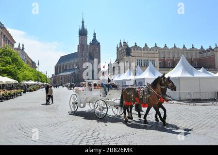 Krakow, Polen - 25. Mai 2019: Pferdekutschen und Wandertouristen am Hauptplatz in Krakow an einem Sommertag, Polen. Zwei Pferde im altmodischen Coach Stockfoto