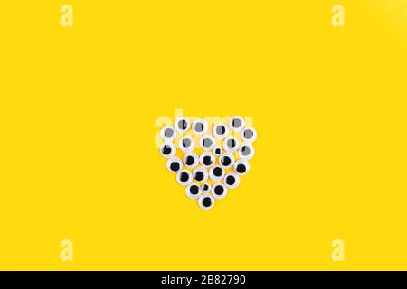 Herzform aus Googly Kunststoffaugen auf gelbem Hintergrund. Verwendet für die Nachahmung von Augäpfeln für handhandwerkliche Spielzeuge und Puppen und andere Kreativität. Flach Stockfoto