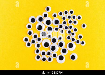 Googly plastische Augen auf gelbem Hintergrod. Verwendet für die Nachahmung von Augäpfeln für handhandwerkliche Spielzeuge und Puppen und andere Kreativität. Flaches Lay. Stockfoto