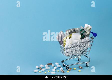 Verschiedene Kapseln, Tabletts und Medikamente im Einkaufswagen und Pillen, die aus der weißen Flasche auf blauem Grund verschüttet werden. Kauf- und Einkaufskonzept für die Medizin. Stockfoto