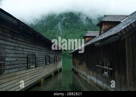 Bootshaus / Bootshäuser am Königssee (Nationalpark Berchtesgaden), umgeben von Bergen und Wolken. Holzhütten am See. Stockfoto