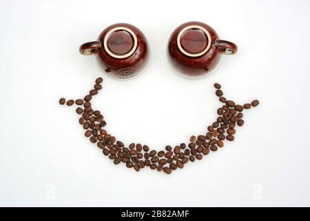 Smiley-Gesicht aus Kaffeetassen und Kaffeebohnen. Fröhliches Gesicht mit Kaffee. Stockfoto