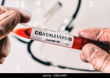 Hände in Handschuhen mit Schlauch mit Coronavirus Covid-19-Etikett, gefüllt mit roter Flüssigkeit (künstlerische Darstellung) Stockfoto