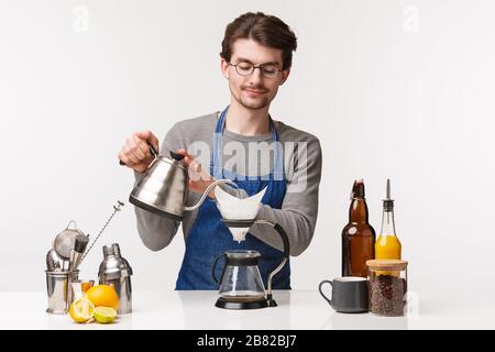 Barista, Café-Mitarbeiter und Barkeeper Konzept. Portrait von gutaussehenden jungen männlichen Angestellten, die Filterkaffee zubereiten, der Wasser in den Wasserkocher gießt, zärtlich lächelnd Stockfoto