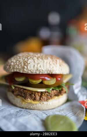 Nahansicht eines quorn-burgers auf einem Holztisch. Einige Ketchup, Senf, veganer Käse und etwas Salat begleiten das fleischlose Fleisch. Stockfoto