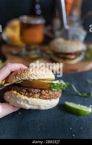 Köstlicher Closeup veggie quorn Burger. Hinten gibt es einen weiteren veganen Burger, einen Bierbecher, Pommes und mehr. Stockfoto