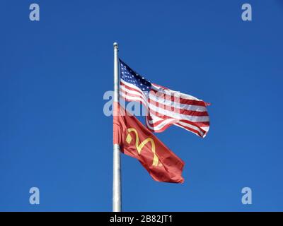 Nahaufnahme von Flagpole gegen blauen Himmel unter amerikanischer Flagge und Flagge mit Logo des McDonald's-Konzerns, Dublin, Kalifornien, 23. Februar 2020. () Stockfoto