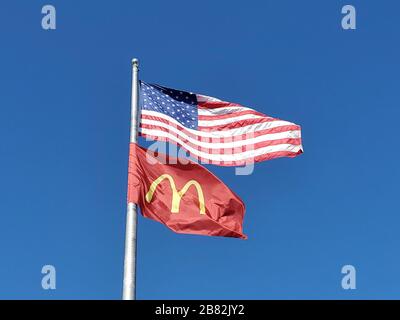 Nahaufnahme von Flagpole gegen blauen Himmel unter amerikanischer Flagge und Flagge mit Logo des McDonald's-Konzerns, Dublin, Kalifornien, 23. Februar 2020. () Stockfoto