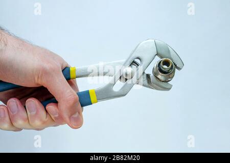 Die Kupplung wird in Zange gespannt. Verstellbarer Schraubenschlüssel. Die Hand hält das Klempnerwerkzeug. Stockfoto