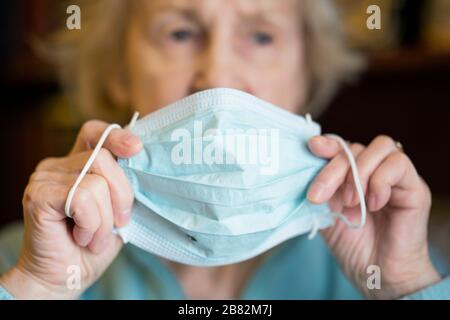 Ältere ältere ältere kaukasische Frau, die eine medizinische prozedurale Gesichtsmaske zum Schutz vor COVID-19, Coronavirus Infektion, aufsetzt Stockfoto