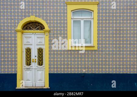 Portugal, Fassade eines Hauses mit typischen Keramikazulejos-Fliesen und einer verzierten Holztür in Weiß und Gelb Stockfoto