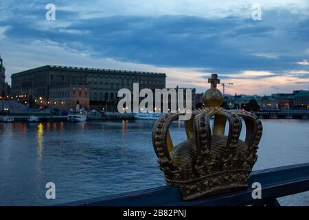 Das Brückengeländer ist mit einer Krone verziert. Die Brücke steht vor dem Königspalast in Stockholm, Schweden. Foto, das während eines Sommer-Sonnenuntergangs aufgenommen wurde. Stockfoto