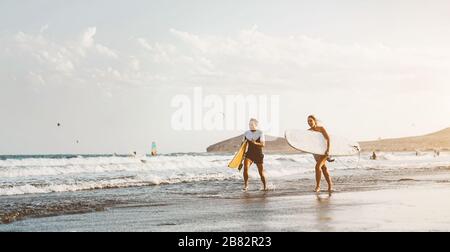 Surferpaar, die lange Meeresufer laufen und bereit sind, auf hohen Wellen zu surfen - sportliche Freunde, die während des Surftags im Meer Spaß haben Stockfoto