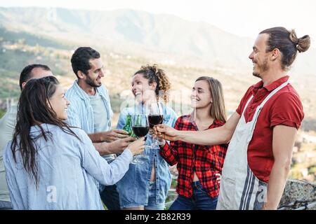Eine Gruppe glücklicher Freunde, die mit Rotweingläsern auf der Terrasse jubeln und toben - junge Leute haben Spaß beim Essen auf der Terrasse Stockfoto