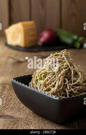 Ein Teller glutenfreier Pasta mit Zucchini, Zwiebel, Käse und Pfeffer auf einem Holztisch. Stockfoto