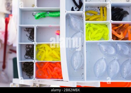 Nahaufnahme von Angelzubehör, Luren, Würmern, Haken in Kunststoff-Tackle-Box Stockfoto