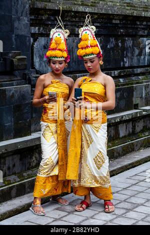 Zwei junge balinesische Hindu-Weibchen, die ein Handy (Handy) bei der Zeremonie Batara Turun Kabeh, Besakih-Tempel, Bali, Indonesien, ansehen. Stockfoto