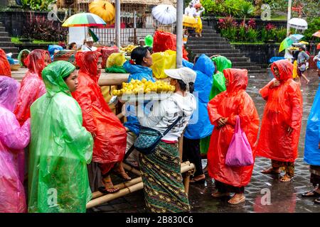 Lokale Frauen, die Sweetcorn/Corn an Besucher verkaufen, die Ponchos während EINER Regendusche tragen, die Batara Turun Kabeh Zeremonie, Besakih Tempel, Bali, Indonesien. Stockfoto