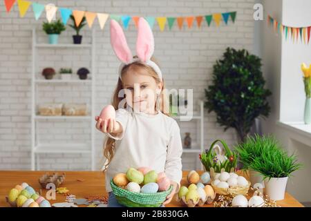 Frohe Ostern. Ein kleines Mädchen mit Hünenähren hält ostereier in den Händen in einem dekorierten Raum. Stockfoto
