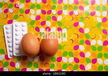 Zwei Hühnereier und weiße Pillen auf einem farbenfrohen, blütenförmigen, benutzerdefinierten gelben Hintergrund. Konzept von ostern und Pillen, ostern unter Korona-Situation, Chi Stockfoto