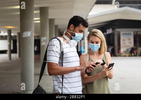 Kaukasische Paare unterwegs, die eine Kovid19-Coronavirus-Maske tragen und ihre Telefone betrachten Stockfoto