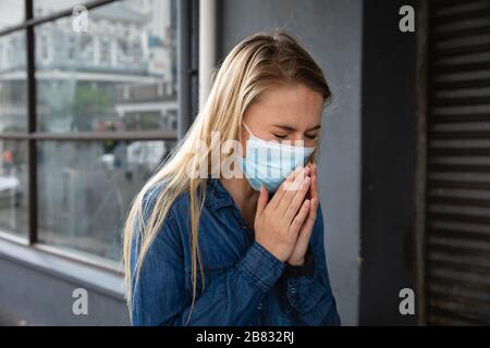 Kaukasische Frau, die außen eine kovidierende 19-Coronavirus-Maske trägt und hustet Stockfoto